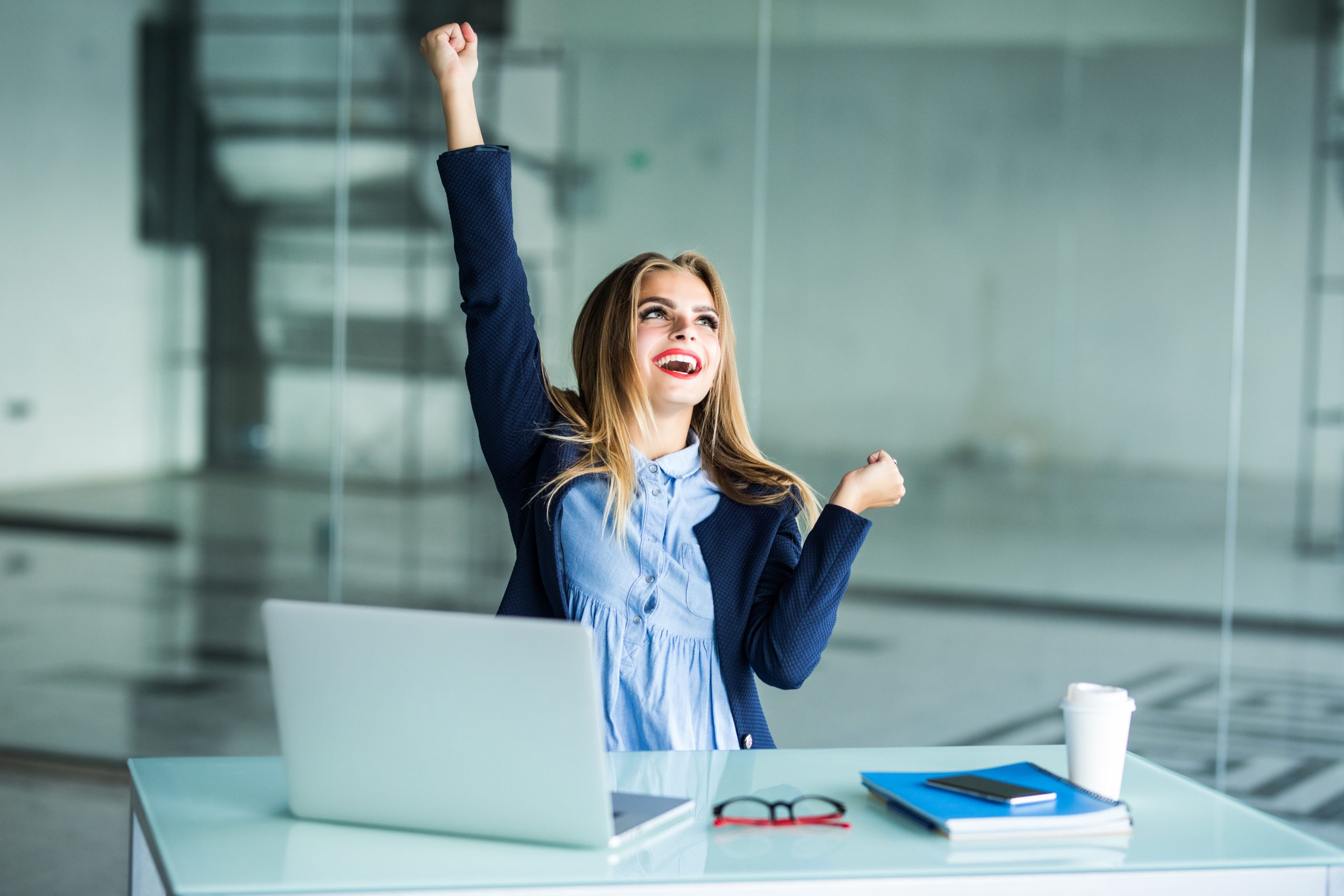 Successful young business woman with arms up at the office